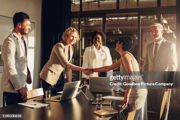 two businesswomen shaking hands together after a successful boardroom meeting - mergr stock pictures, royalty-free photos & images