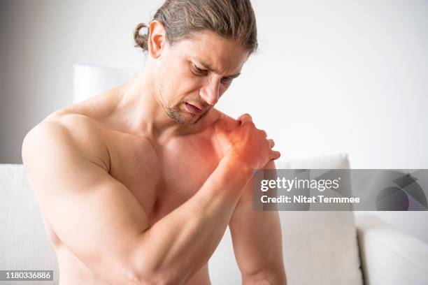 handsome young man feeling the pain in shoulder while exercising at home. - man touching shoulder stock pictures, royalty-free photos & images