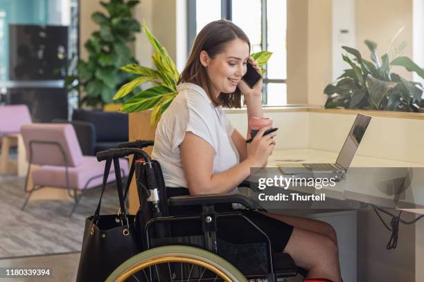 young woman in wheelchair working in modern office - wheelchair access stock pictures, royalty-free photos & images