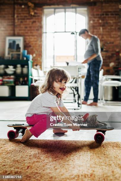 young girl playing with skateboard while mother works from home - indoor skating stock pictures, royalty-free photos & images
