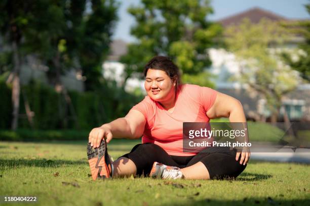 asian overweight woman exercising stretch alone in public park in village, happy and smile in morning during sunlight. fat women take care of health and want to lose weight concept. - fat loss training stockfoto's en -beelden