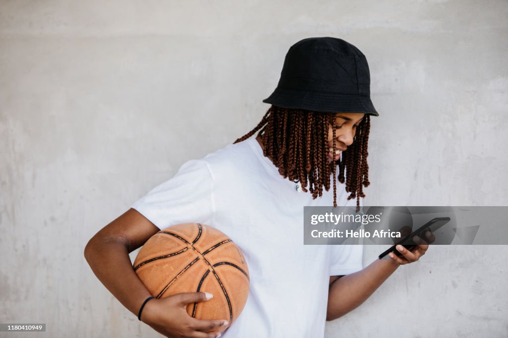 Side view of beautiful young woman reading her phone with basketball under arm