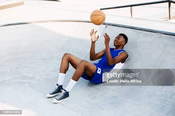 Basketball player relaxing in a skating bowl throwing a ball in the air