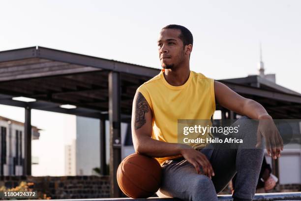 basketball player wearing yellow resting his arm on ball and looking of in profile - arm tattoos for black men fotografías e imágenes de stock
