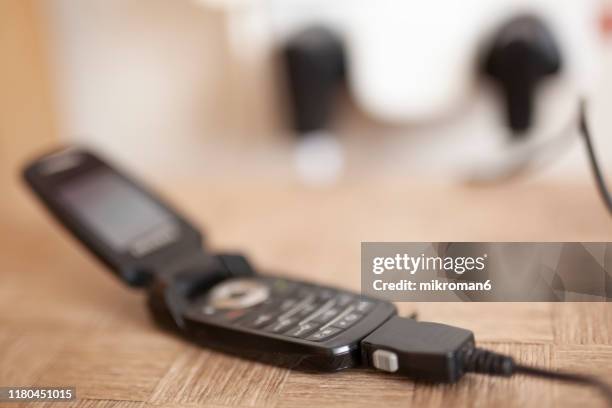 flip phone charging. wall socket in the background - telefone-de-dobrar imagens e fotografias de stock