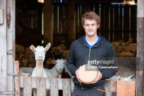 orgullo joven agricultor sosteniendo una ronda de queso entero de cabra - queso de cabra fotografías e imágenes de stock