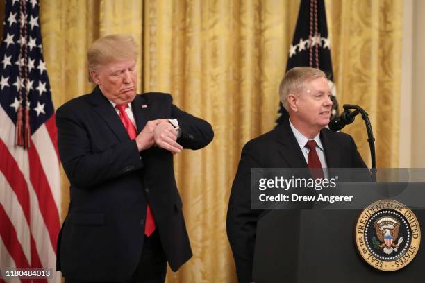 President Donald Trump pretends to check his watch after Sen. Lindsey Graham mentioned upcoming Senate votes during an event about judicial...