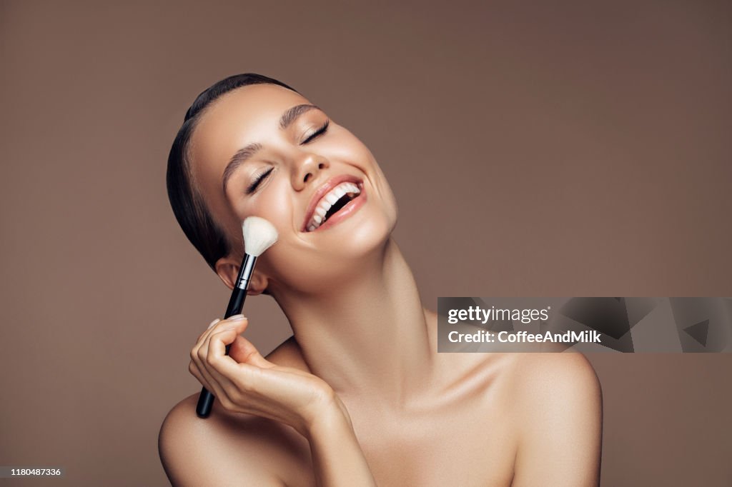 Beautiful young woman applying foundation powder