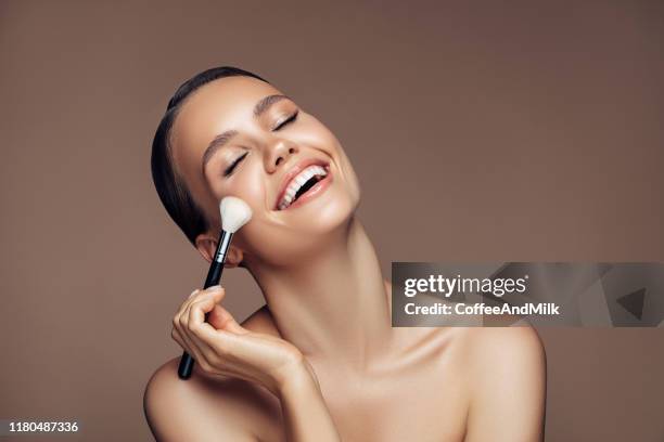beautiful young woman applying foundation powder - woman applying makeup stock pictures, royalty-free photos & images