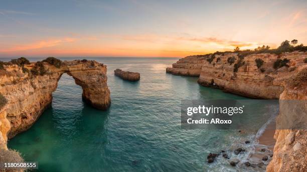 algarve beach at sunset. loving moment under natural arch carved in stone is a tourist attraction of the south coast of portugal. panoramic view from the cliff. - albufeira stock-fotos und bilder