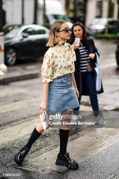 Guest wears a hairpin, earrings, Miu Miu sunglasses, a floral print cream-color puff sleeves top with a hi-neck and a brown lavaliere, a blue denim...