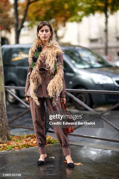 Sylvia Haghjoo wears a brown and burgundy Prince of Wales check jacket, assorted baggy pants, a black and green knit scarf decorated with feathers, a...