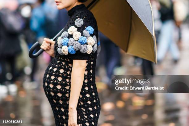 Guest wears a hi-neck crochet openwork black dress with colorful crochet flowers on the puff sleeves, and holds an umbrella, outside Miu Miu, during...