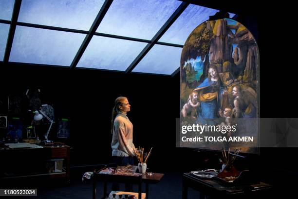 Gallery worker poses with a projection of the painting, 'The Virgin of the Rocks' by Leonardo da Vinci in a reimagined studio room during a photocall...