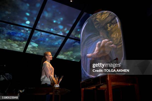 Gallery worker poses with a projection of the painting, 'The Virgin of the Rocks' by Leonardo da Vinci in a reimagined studio room during a photocall...