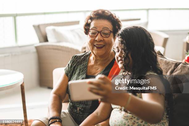grandma with her granddaughter doing a selfie at home - hispanic grandmother stock pictures, royalty-free photos & images