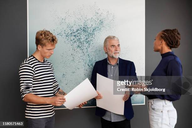 young woman and man talking with mature man in front of art print - art director photos et images de collection