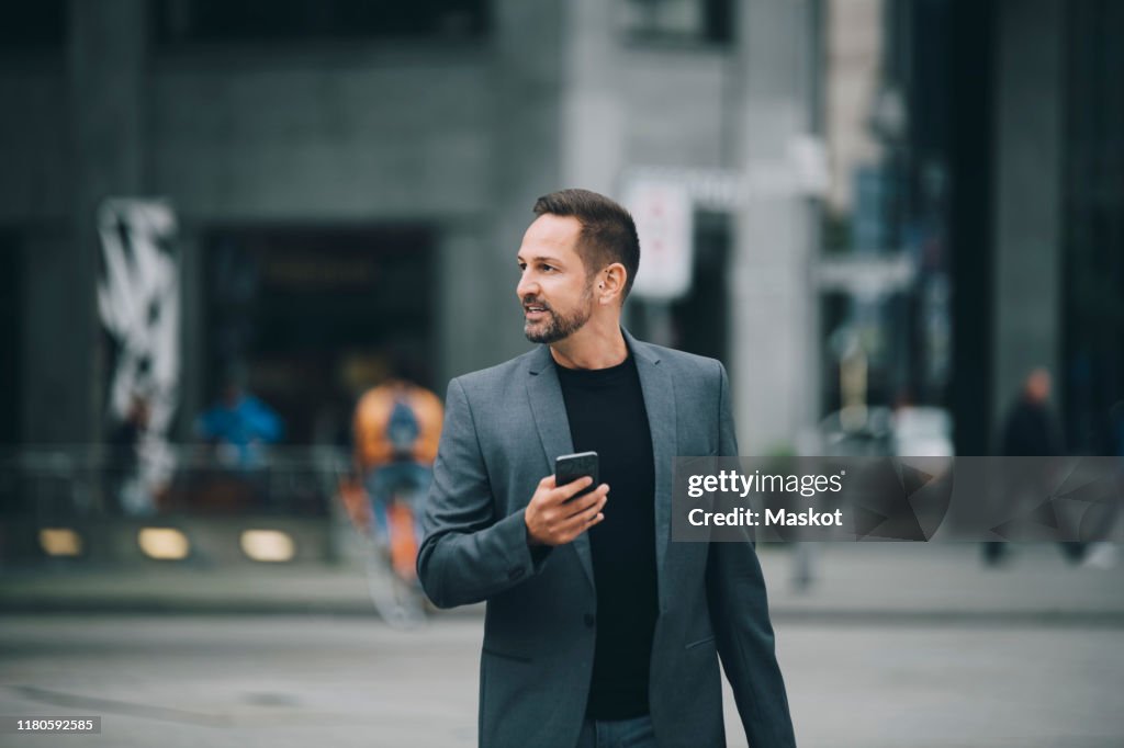 Confident businessman looking away while walking on street in city