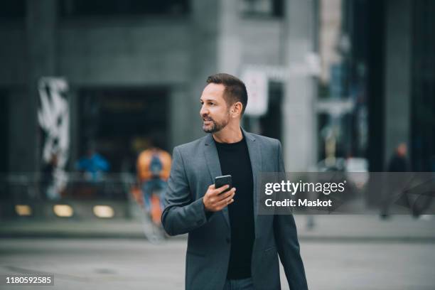 confident businessman looking away while walking on street in city - blazer jacket stockfoto's en -beelden