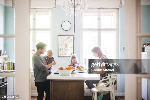 father playing with son while standing by girl and woman busy at kitchen island - family at kitchen fotografías e imágenes de stock