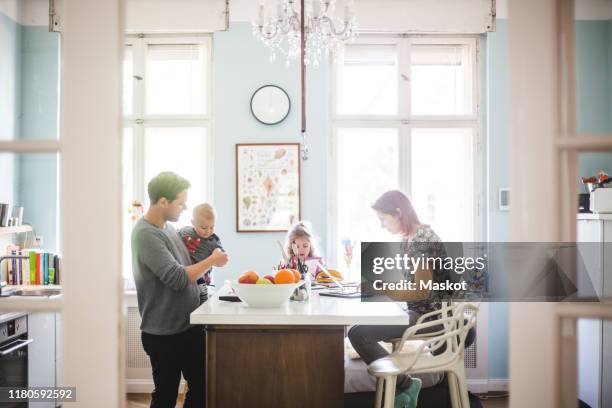 father playing with son while standing by girl and woman busy at kitchen island - brightly lit 個照片及圖片檔