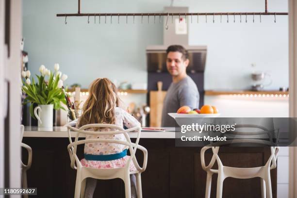 father looking at daughter studying while sitting in kitchen - kitchen island stock pictures, royalty-free photos & images
