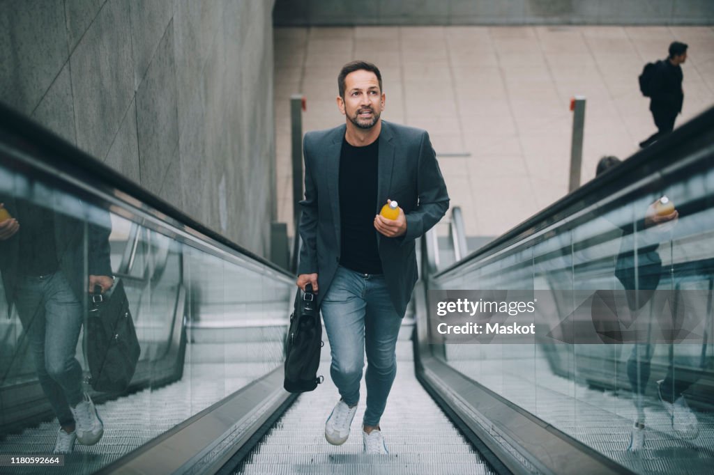 Confident businessman holding drink while moving on escalator in subway