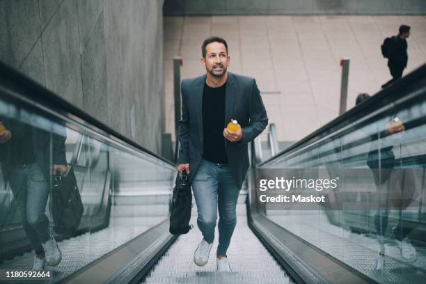 confident businessman holding drink while moving on escalator in subway - hinauf bewegen stock-fotos und bilder