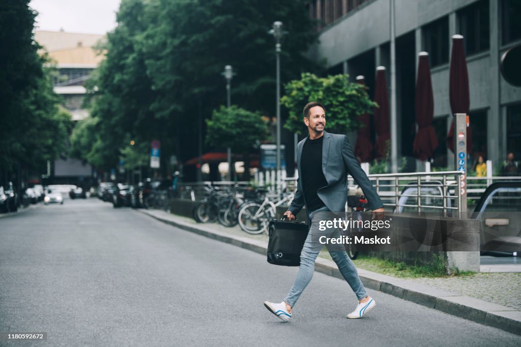 Full length of confident businessman looking away crossing street in city