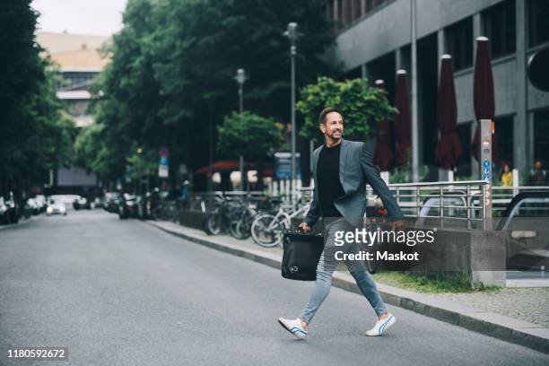 full length of confident businessman looking away crossing street in city - gehen stock-fotos und bilder