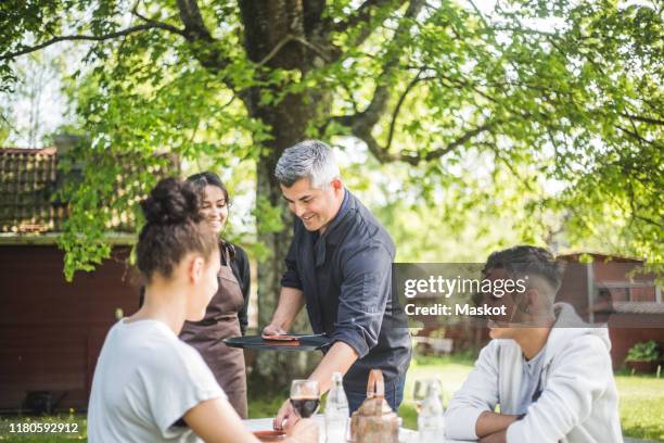smiling owner teaching waitress while customers sitting at table in restaurant - kellner tablett stock-fotos und bilder