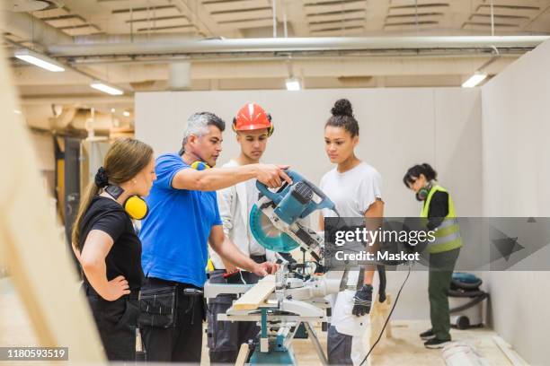 trainees watching confident male carpenter cutting with electric saw in workshop - trainee stock pictures, royalty-free photos & images