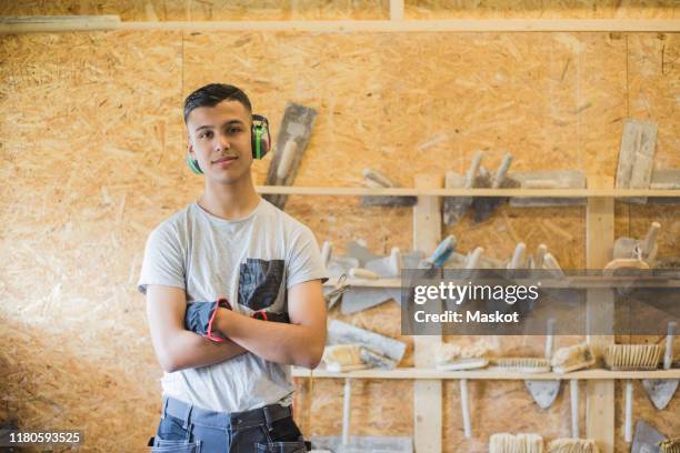 portrait of confident teenage trainee standing with arms crossed against wall at workshop - stage set stockfoto's en -beelden