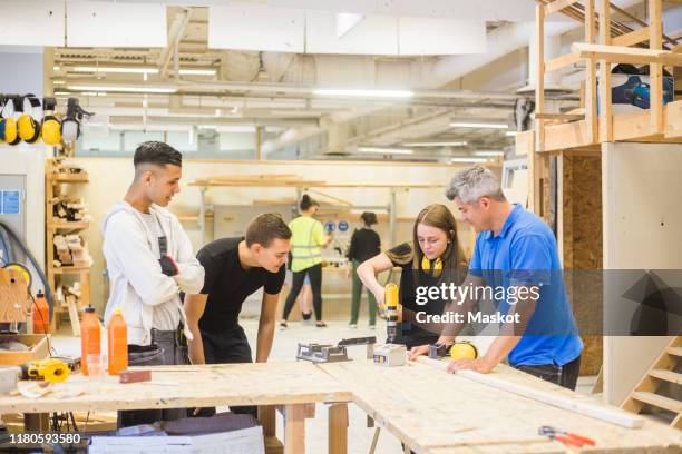 male instructor and trainees watching while woman using power drill at workbench during training - ausbildung und tischler stock-fotos und bilder