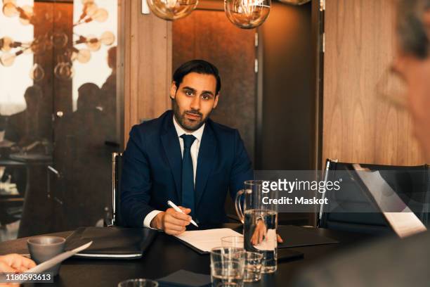 portrait of confident mid adult lawyer with documents at conference table in law office - lawyers serious stock pictures, royalty-free photos & images