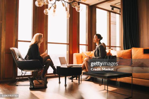 full length of female lawyers discussing while sitting by window at office - legal assistance stock pictures, royalty-free photos & images