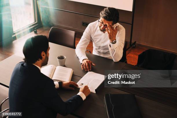 high angle view of male lawyer showing file to mature stressed client at board room in law office - will files stock pictures, royalty-free photos & images