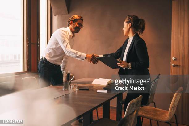 female lawyer shaking hands with male customer after meeting at table in office - lawyer handshake stock pictures, royalty-free photos & images