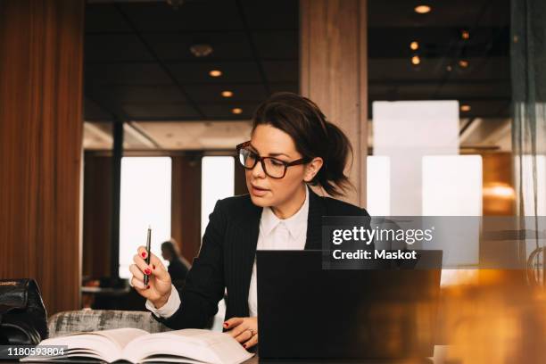 female lawyer with laptop concentrating while reading book at office - legal system foto e immagini stock