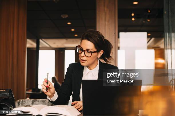 female lawyer with laptop concentrating while reading book at office - law office stock pictures, royalty-free photos & images