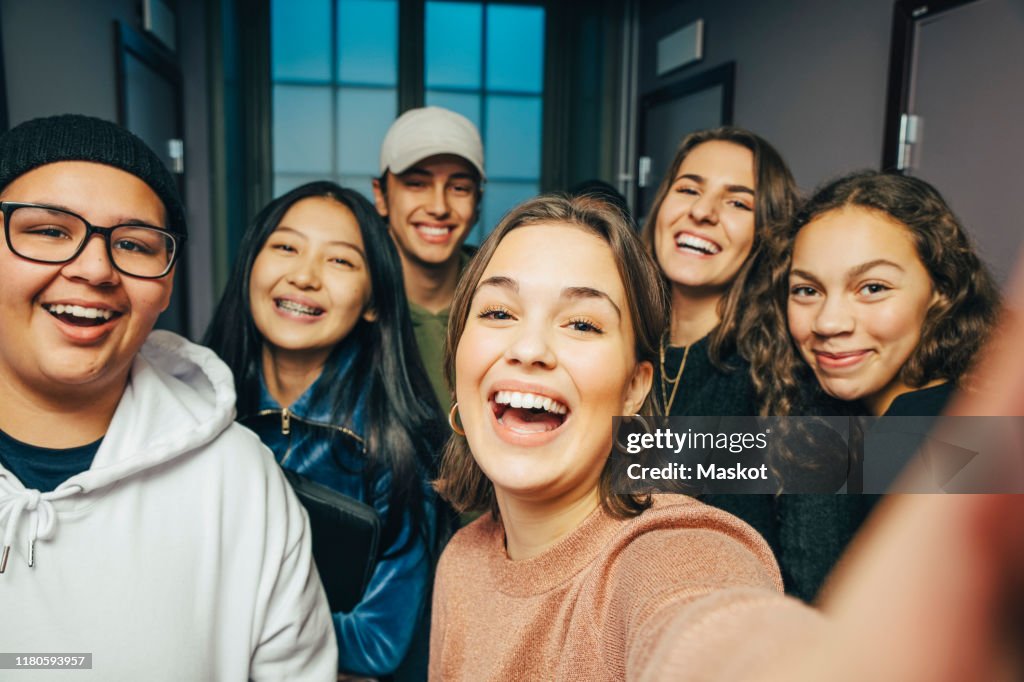Cheerful teenage classmates taking selfie in corridor