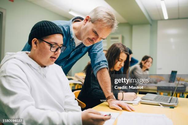 male teacher assisting student at desk in classroom - high school teacher stock pictures, royalty-free photos & images