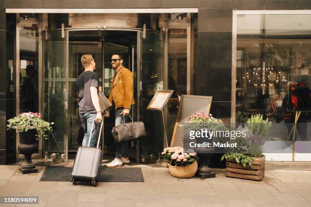 friends talking while standing at doorway of hotel in city - hotel stadt stock-fotos und bilder