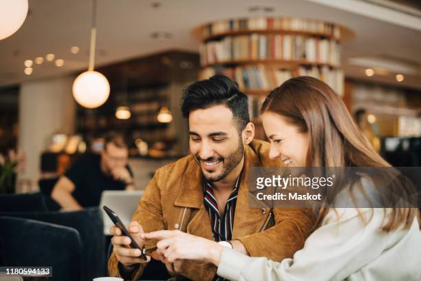smiling couple using smart phone while sitting in restaurant - phone a friend stock pictures, royalty-free photos & images