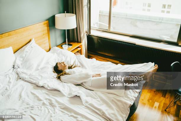 smiling woman in bathrobe having fun on bed at hotel room - hotel stock-fotos und bilder