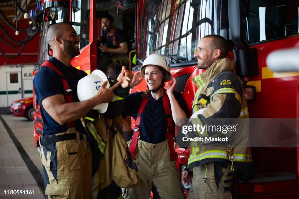 happy firefighters discussing while standing by fire truck in fire station - firefighter fotografías e imágenes de stock