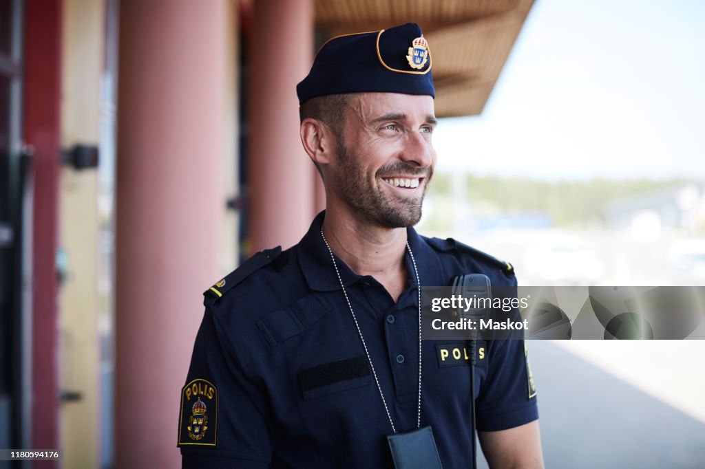 Happy policeman looking away while standing outside police station