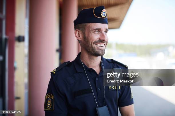 happy policeman looking away while standing outside police station - civil servant stock-fotos und bilder