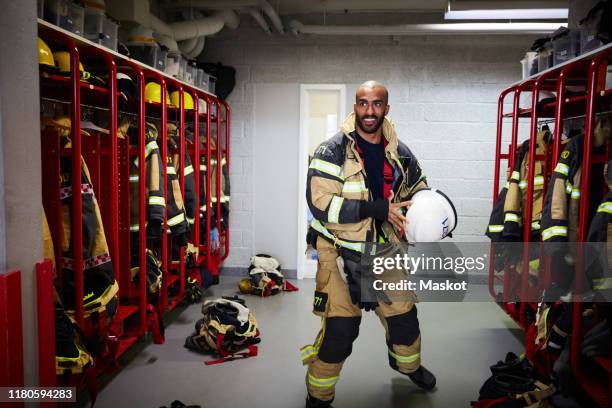 male firefighter holding work helmet in locker room at fire station - firefighter getting dressed stock pictures, royalty-free photos & images