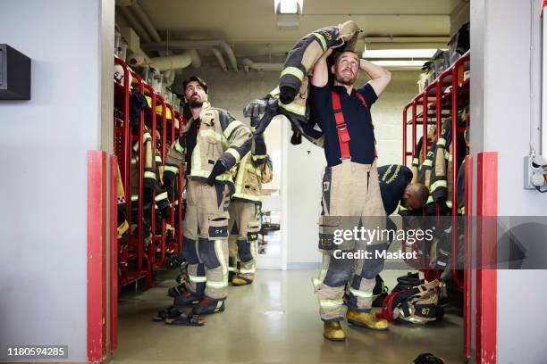 firefighters wearing protective workwear in locker room while looking up at fire station - caserne photos et images de collection